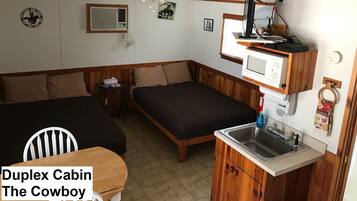 A duplex cabin with a kitchenette, two beds, a ceiling fan, and a mounted TV.