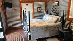 Un dormitorio rústico con una cama de estructura metálica, un letrero de bienvenida, un televisor y un cuadro en la pared.
