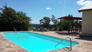 Una piscina rectangular con borde de piedra, una escalera metálica y una estructura de toldo rojo.