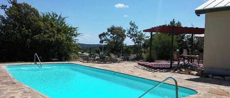 A rectangular swimming pool with a stone border, a metal ladder, and a red canopy structure.