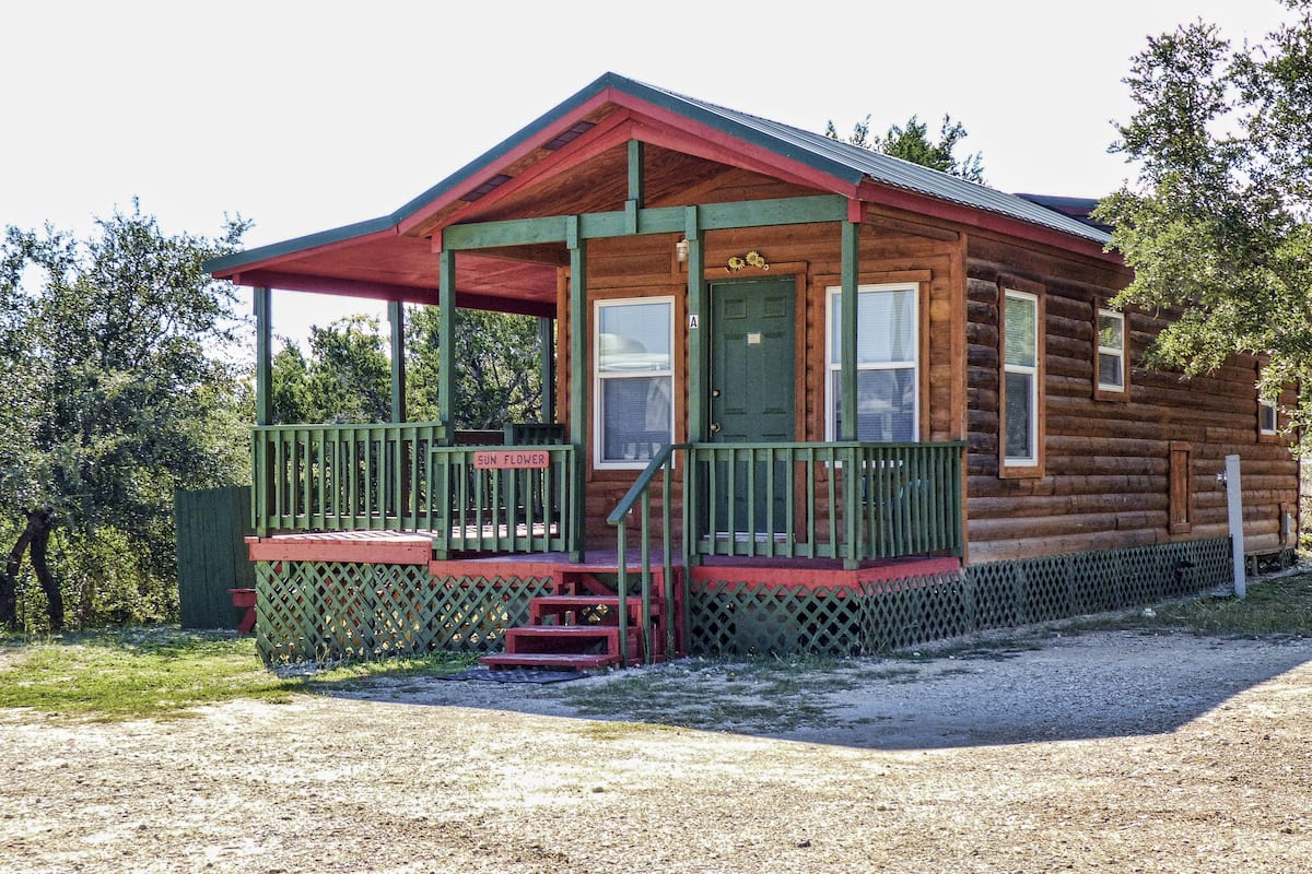 A log cabin with a porch, a front door, and a small set of stairs leading up to the entrance.