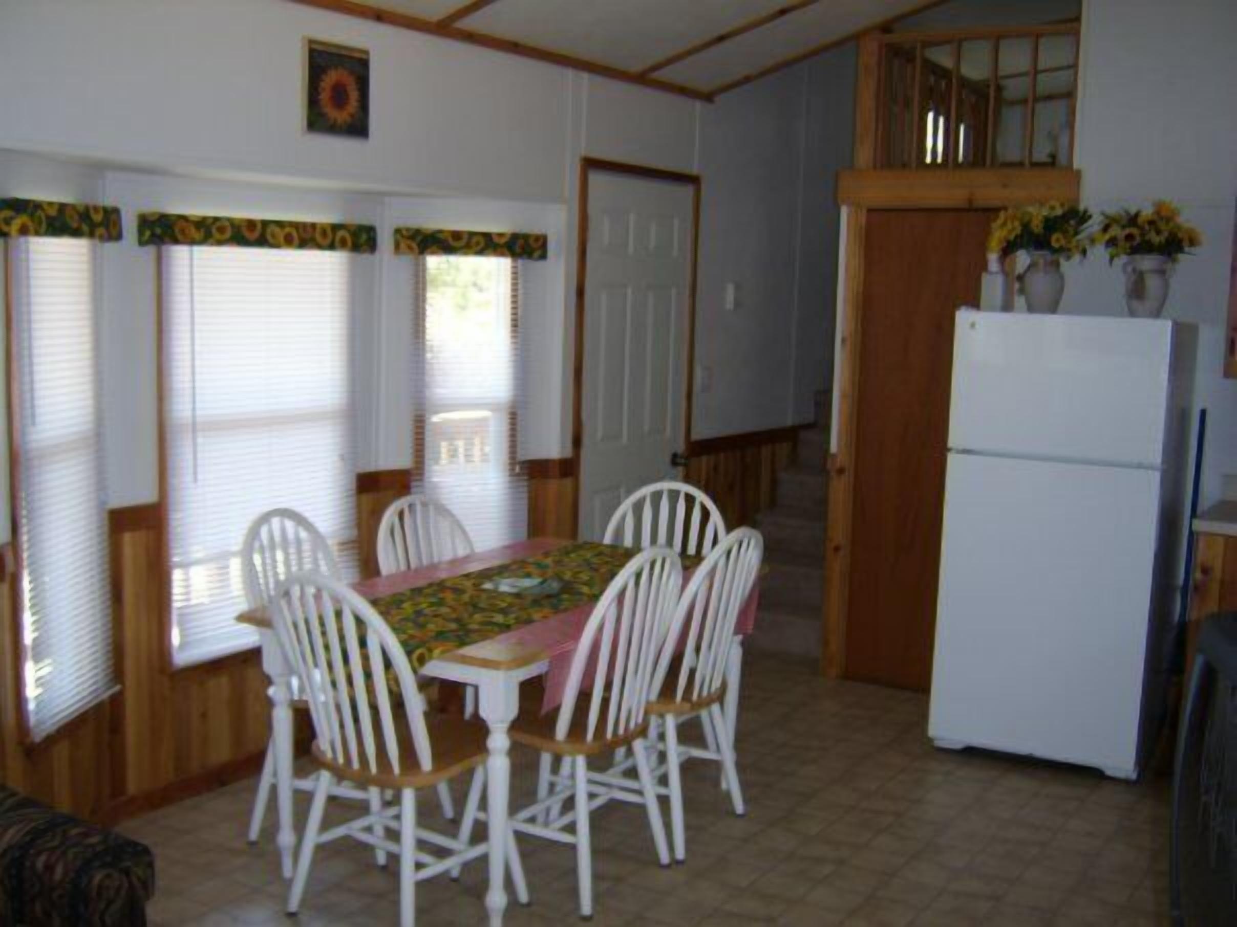 A compact kitchen with a dining table, chairs, a refrigerator, and a window with blinds.