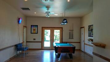 Une pièce spacieuse équipée d’une table de billard, d’un ventilateur de plafond et d’une porte donnant sur un espace extérieur.
