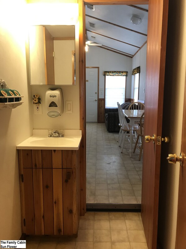 A wooden cabinet with a sink, a Gojo soap dispenser, and a window with a floral curtain. - Top of the Hill RV Resort (Boerne)