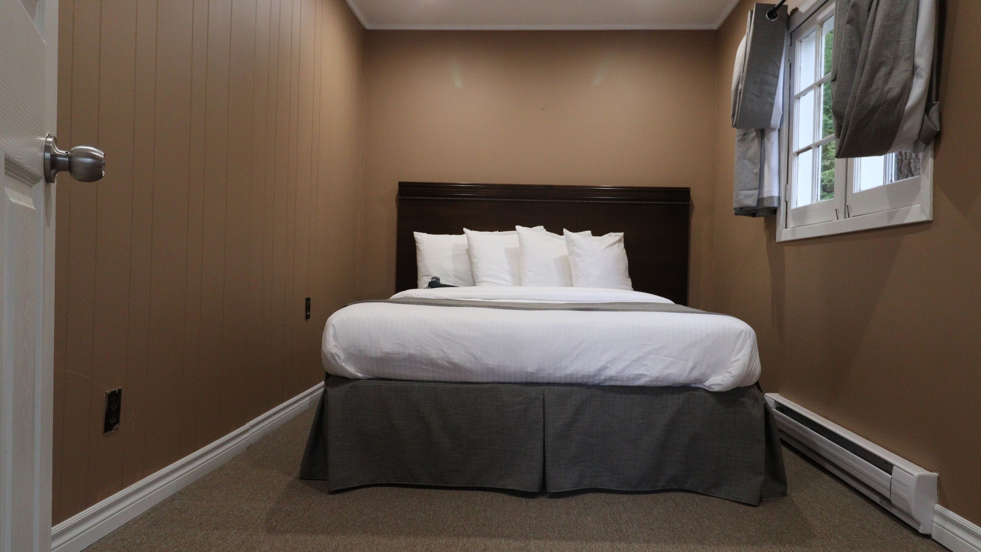 Un dormitorio con cama, cabecera y ventana con cortinas.