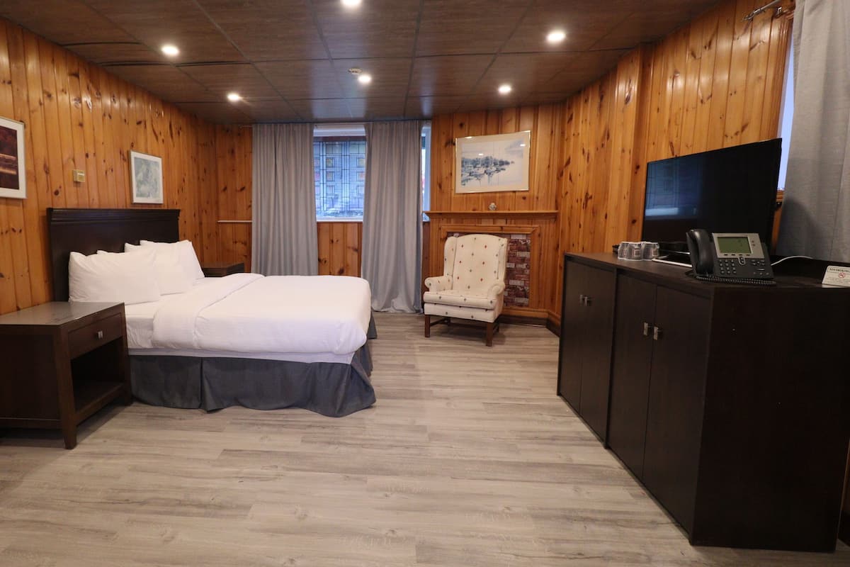 Une chambre d’hôtel avec des murs en bois, un lit avec du linge de maison blanc, un bureau avec un téléphone et un téléviseur posé sur une commode.