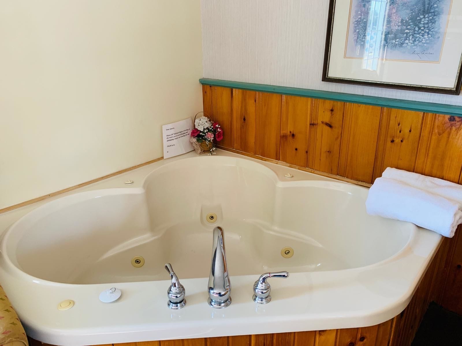 A large freestanding bathtub with three faucets, a small sink, and a framed picture above it.