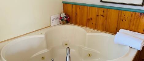 A large freestanding bathtub with three faucets, a small sink, and a framed picture above it.