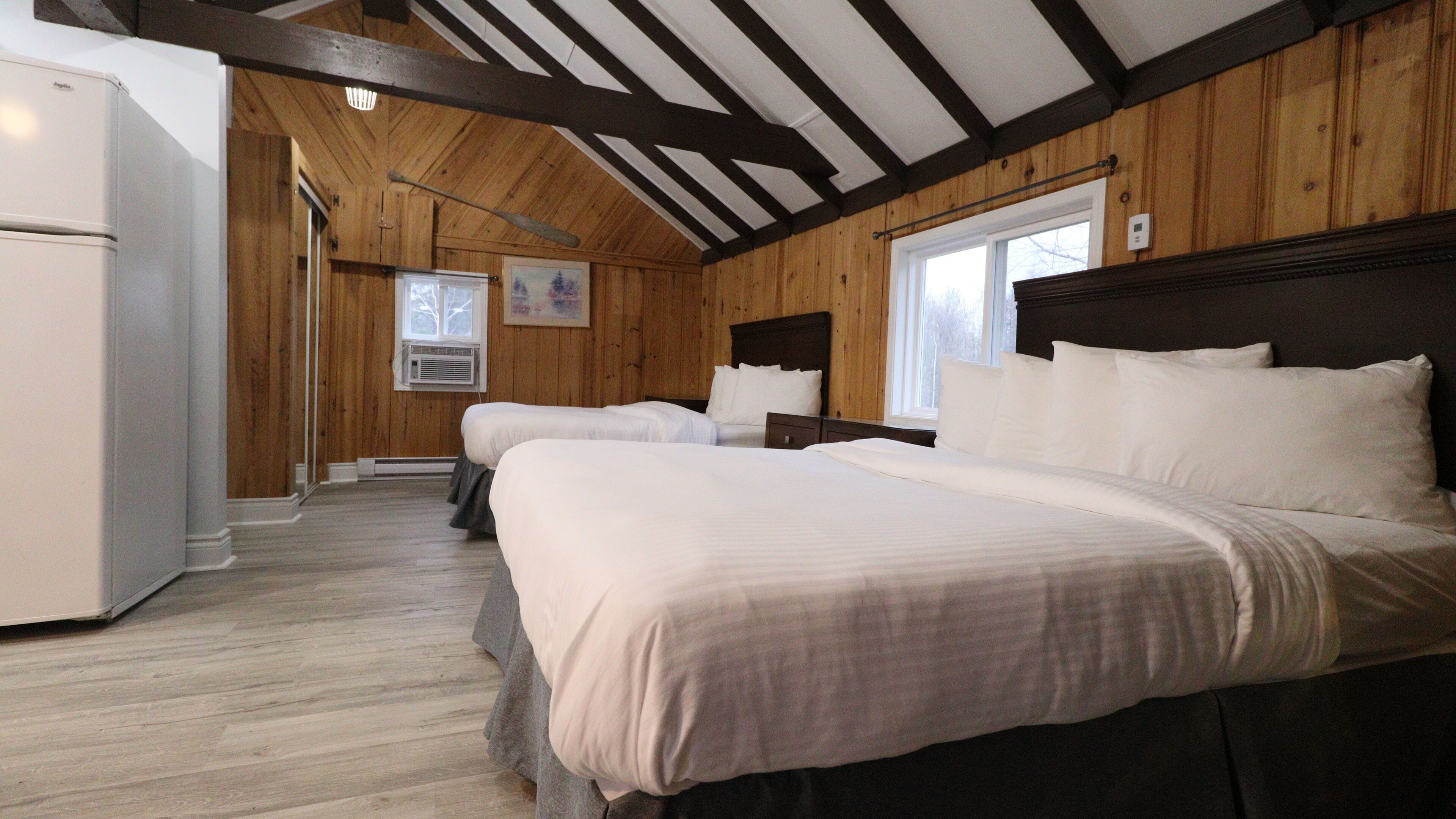 A room with two beds, a refrigerator, wooden walls, and a window.