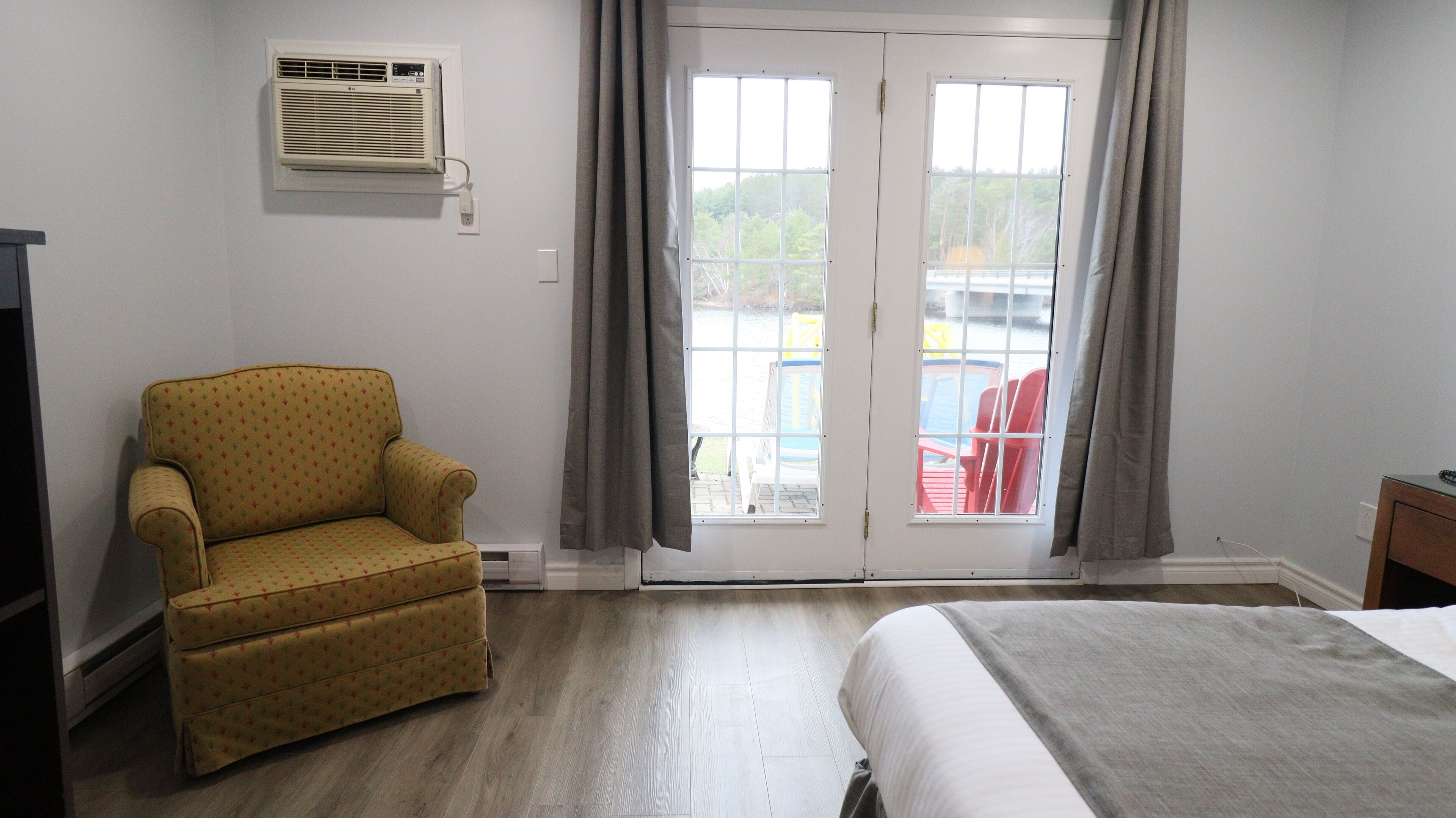 A room with a bed, a chair, a window with curtains, and an air conditioning unit on the wall.