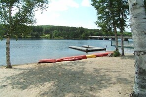 A lakeside view with a dock, a rowboat, and a sandy beach area.