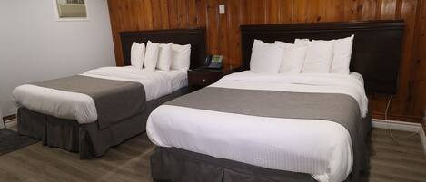 Two double beds with grey bedding, wooden headboards, and a wooden paneled wall.