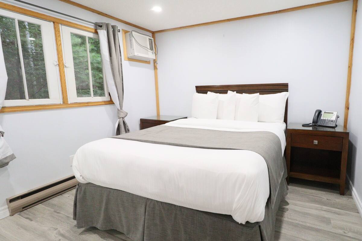 Une chambre d’hôtel avec un grand lit, une table de chevet avec un téléphone, une fenêtre avec des rideaux et un climatiseur fixé au mur.