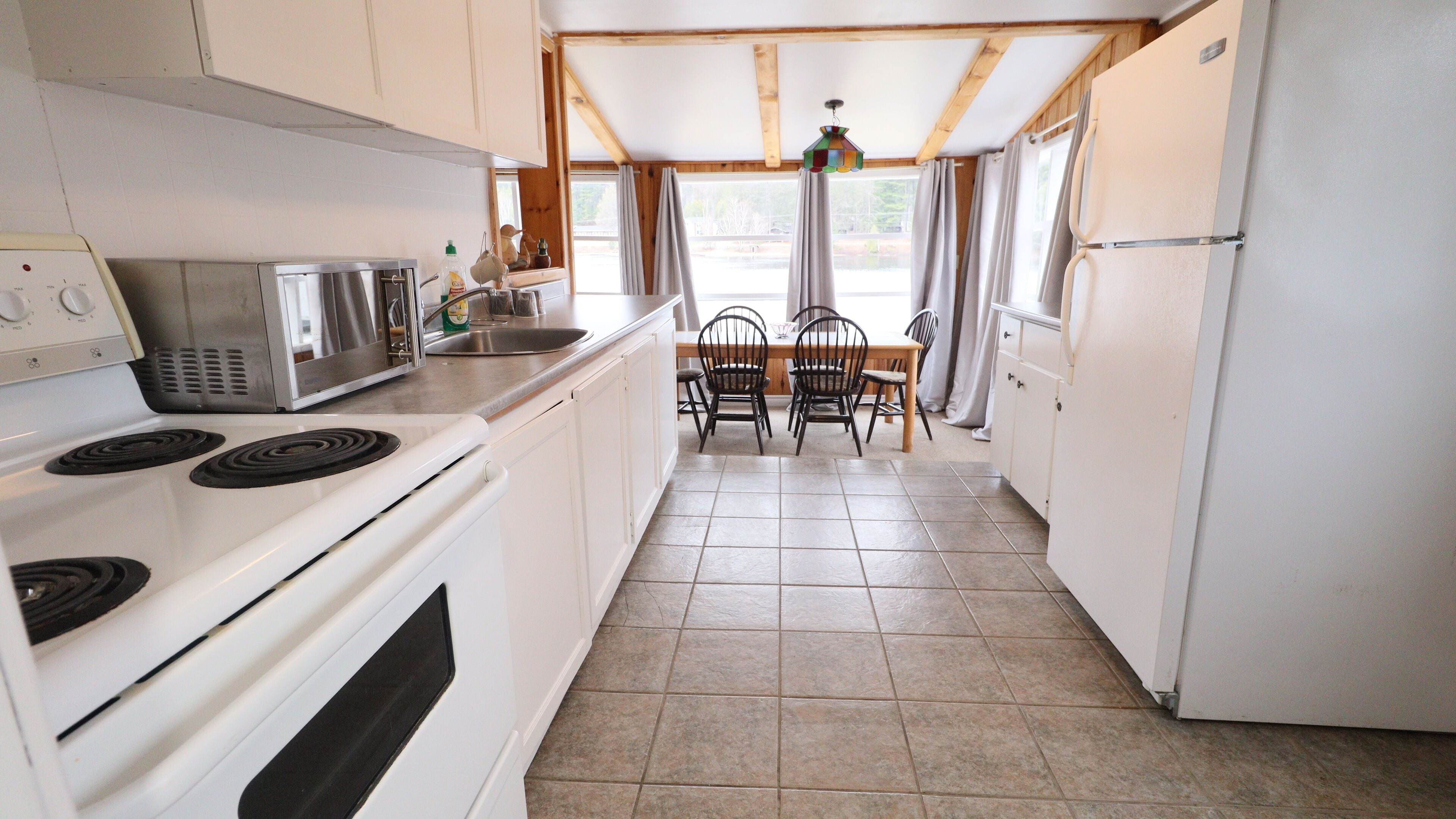 A compact kitchen with white appliances, a dining table with chairs, and a window with curtains.