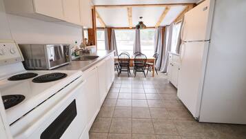 A compact kitchen with white appliances, a dining table with chairs, and a window with curtains.