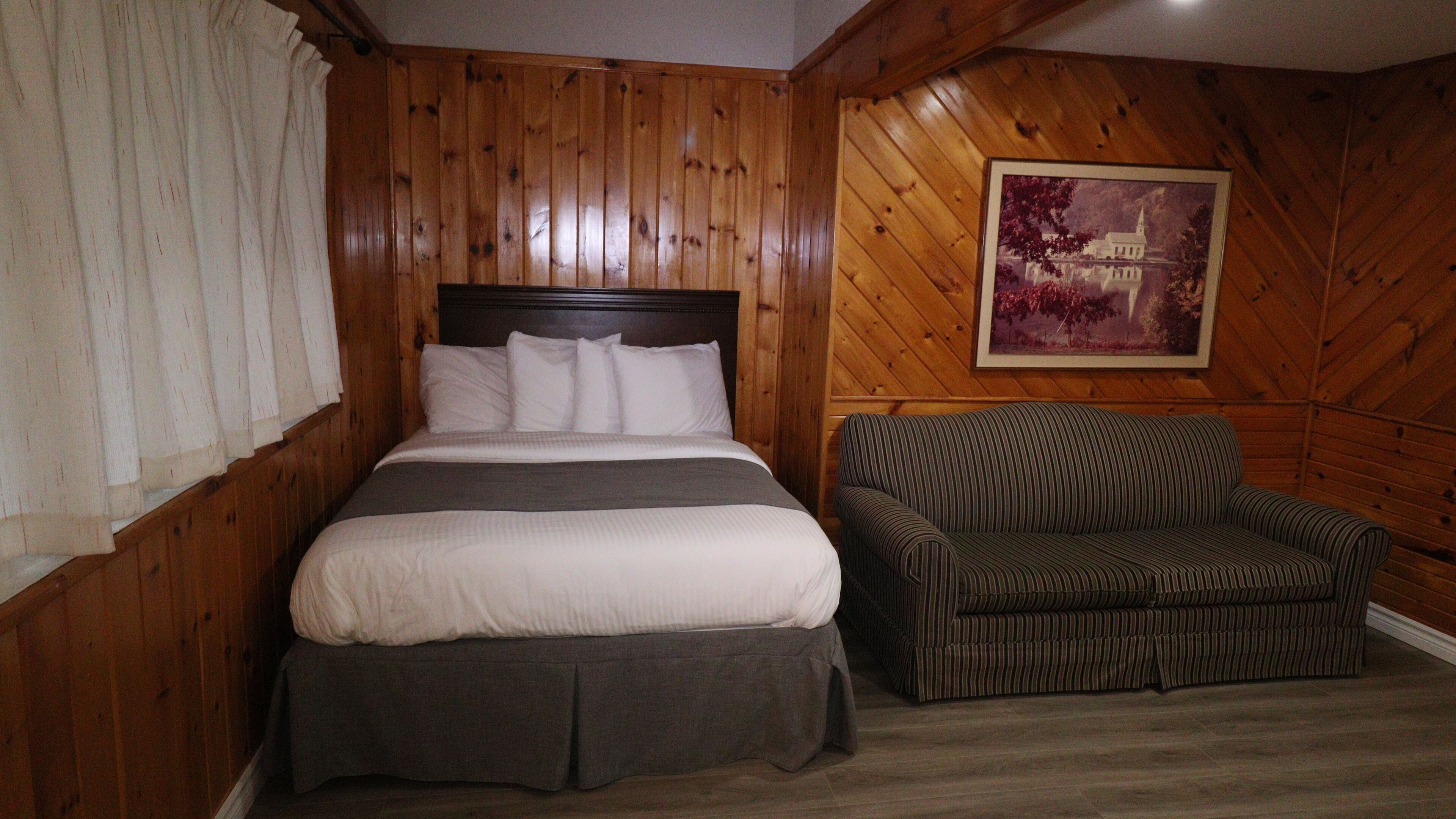Una habitación con un revestimiento de madera, una cama con ropa blanca y un sofá a rayas.