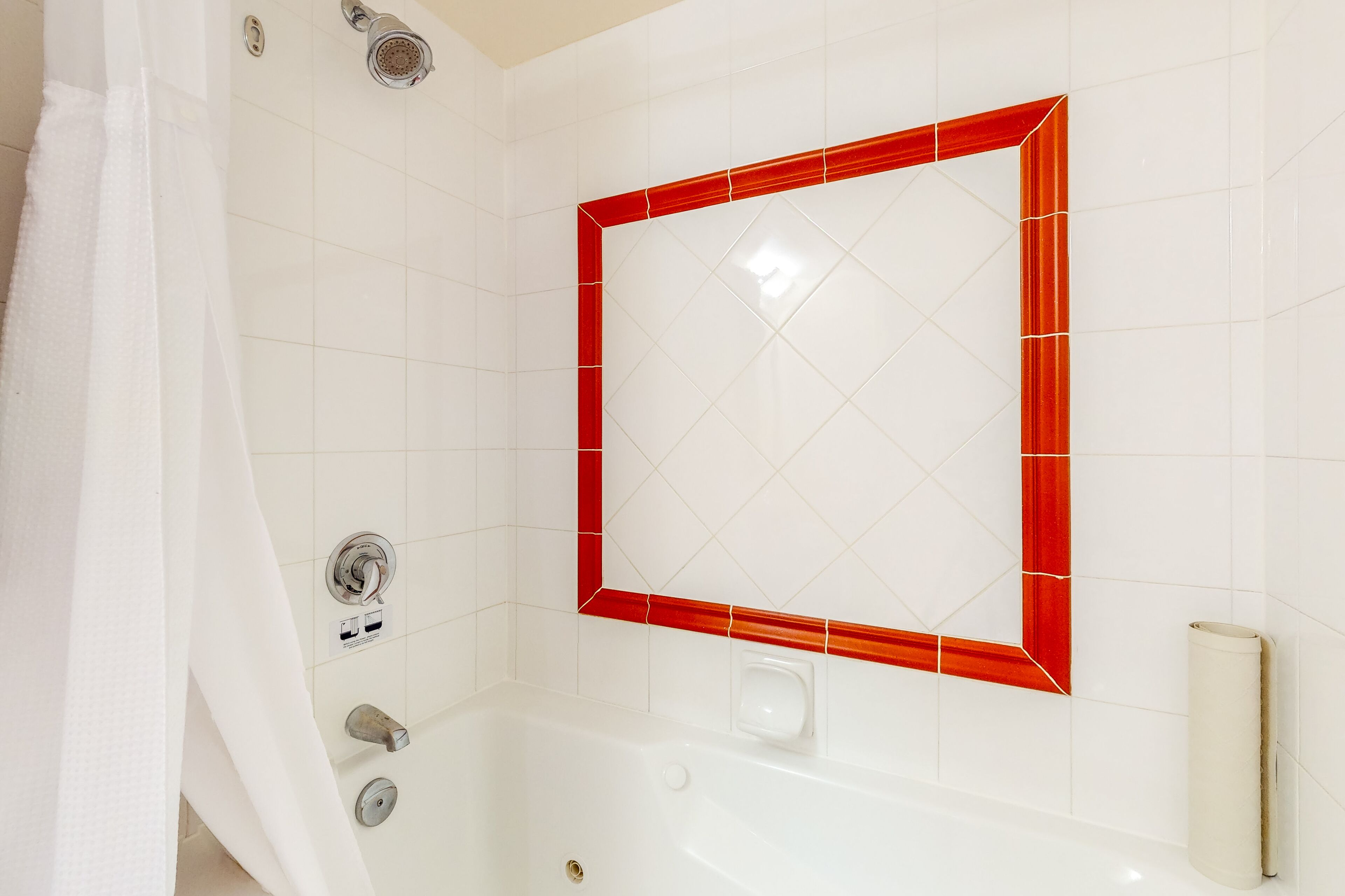Een badkamer met een witte badkuip, een douchegedeelte met rode tegels en een wit toilet.