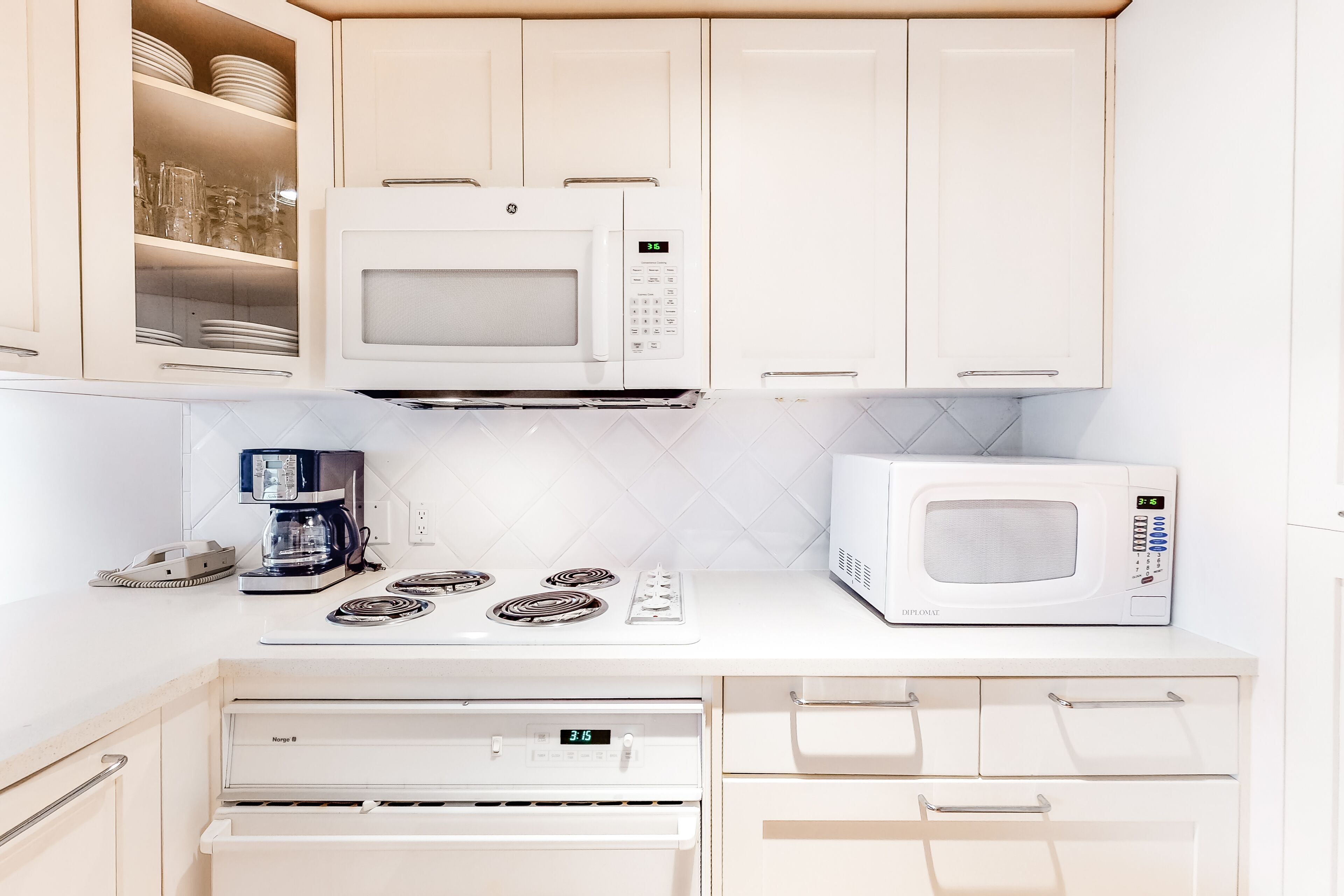 A modern kitchen with white cabinetry, a built-in microwave, a coffee maker, and a stove.