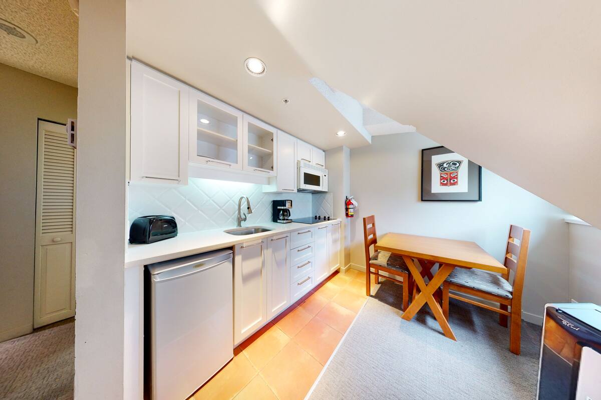 A compact kitchen with white cabinets, a microwave, and a coffee maker. There is a wooden dining table with chairs.