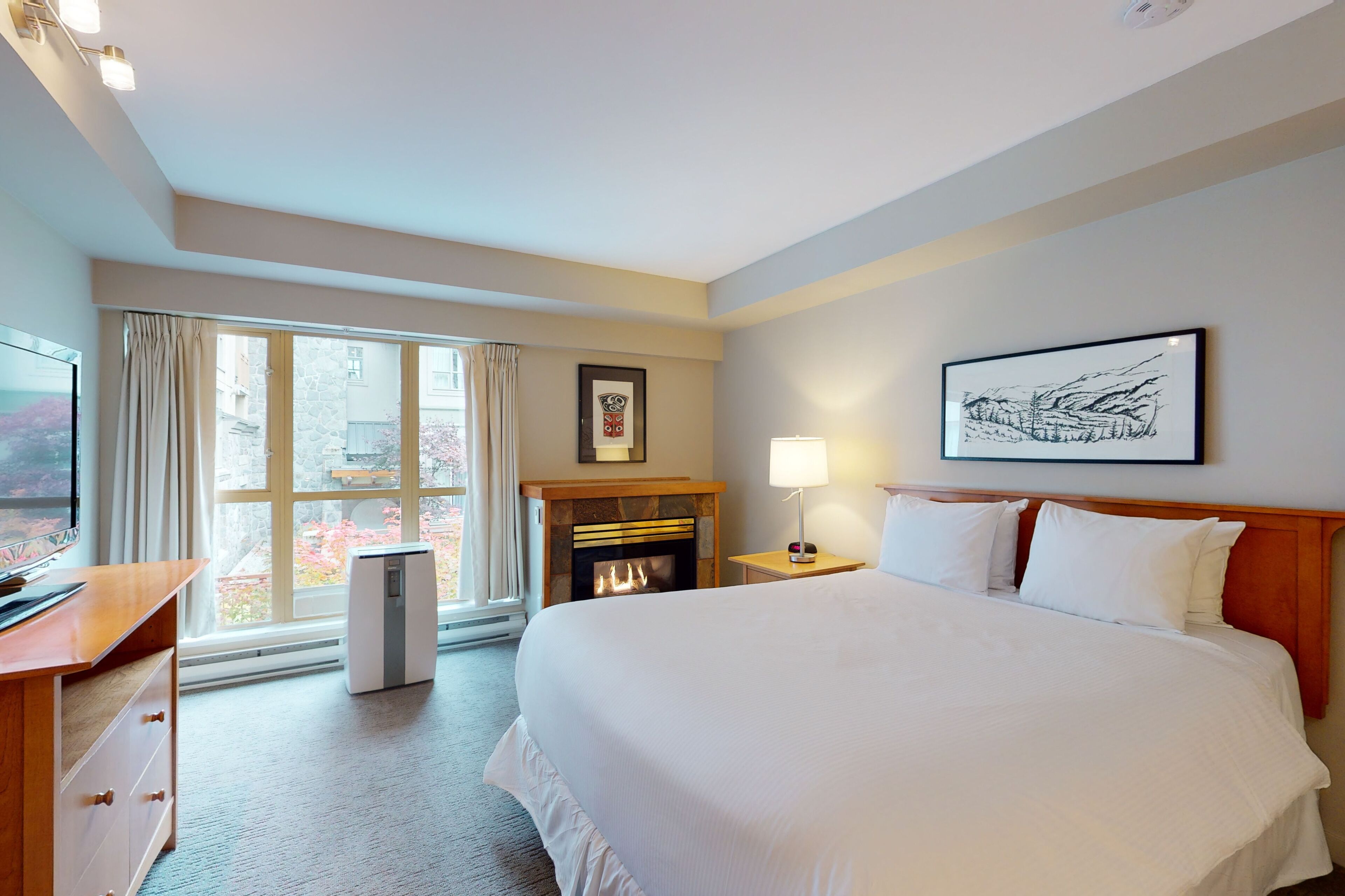 A hotel room with a bed, a desk, a fireplace, and a large window.