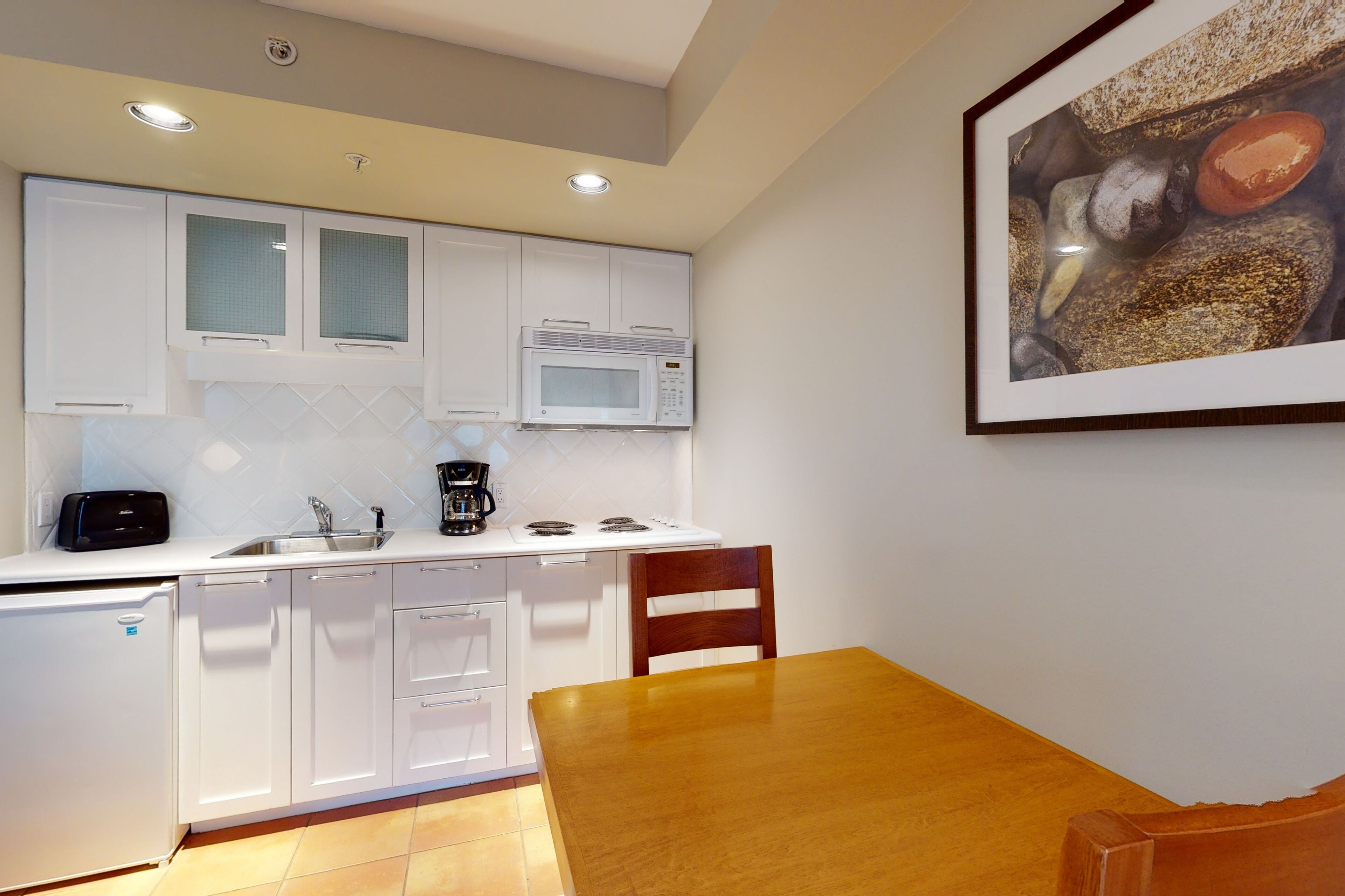 A compact kitchen with white cabinets, a microwave, a coffee maker, and a dining table with chairs.