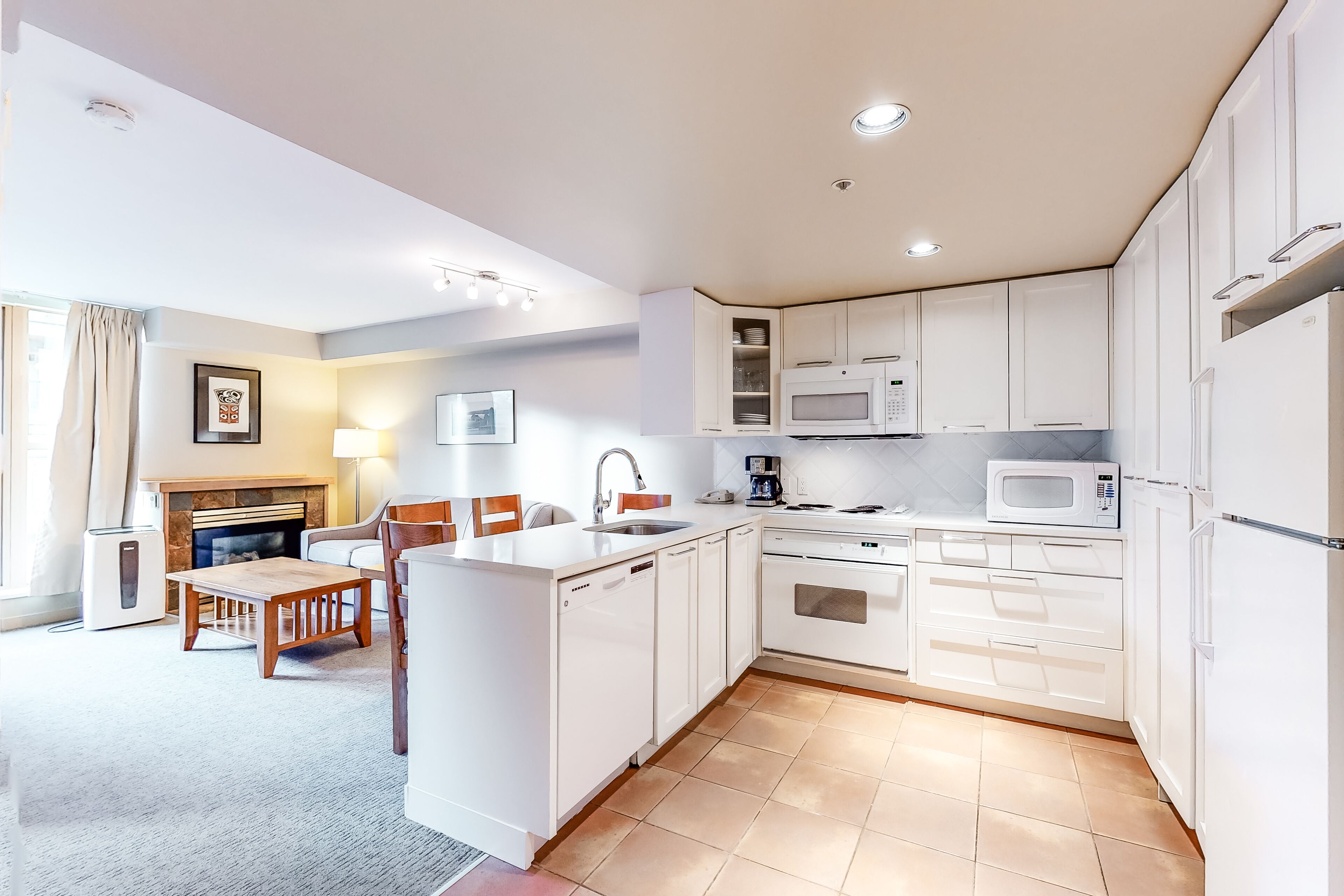 A modern kitchen with white cabinetry, a built-in microwave, and a dining area with a wooden table and chairs.