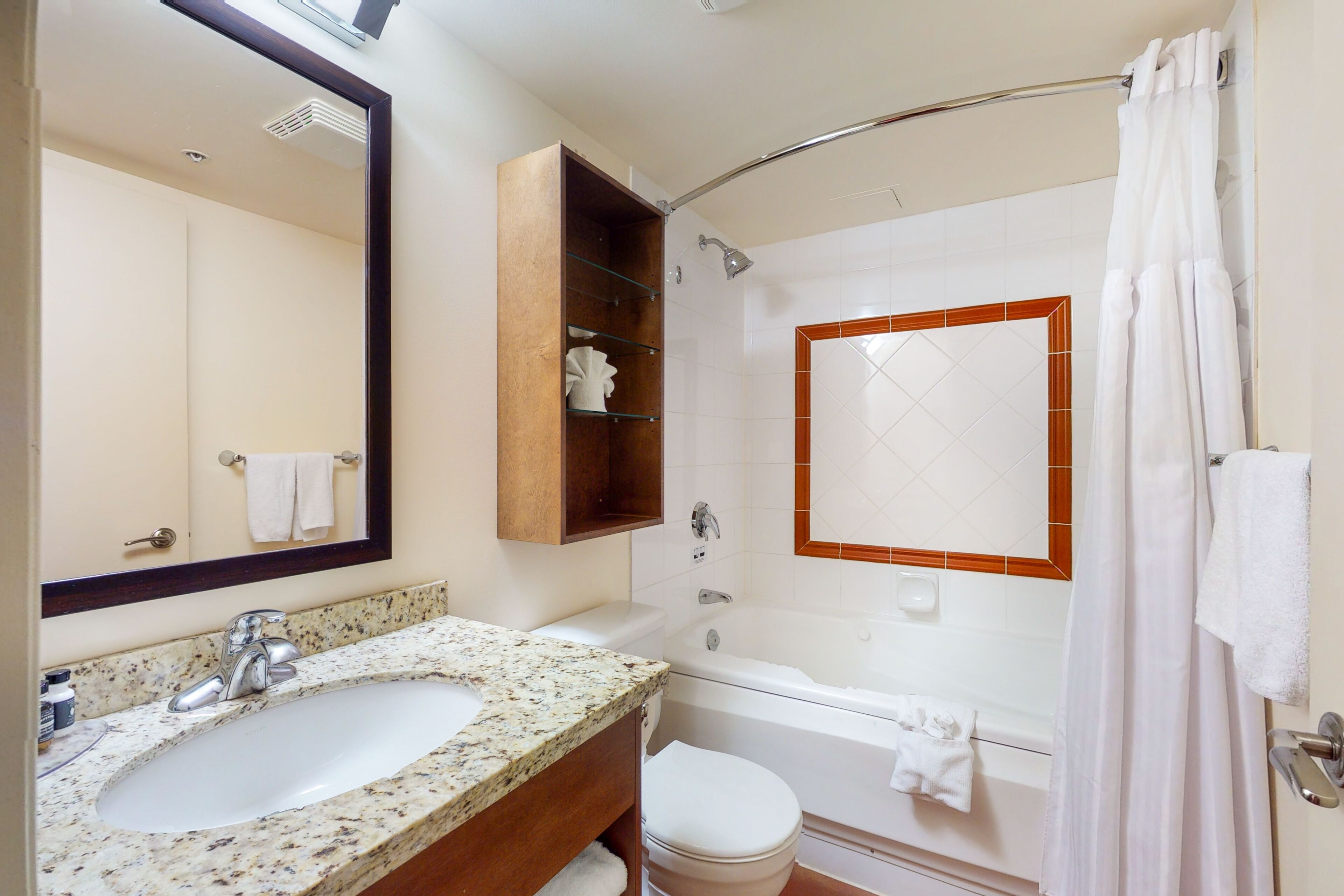 Un baño con lavamanos de granito, espejo, ducha y bañera.