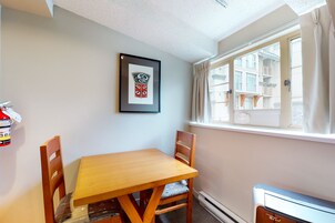 Una habitación con una mesa y sillas de madera, un cuadro en la pared, una ventana con cortinas y un radiador.