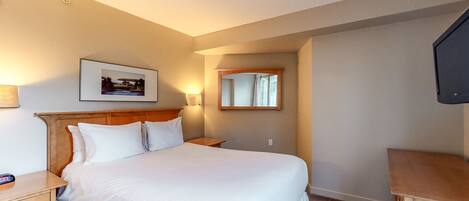 A hotel room with a large bed, a wooden headboard, a bedside table with a lamp, a framed picture on the wall, and a mirror.