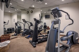 Un gimnasio con diferentes máquinas de ejercicio, un espejo grande y un televisor instalado en la pared.