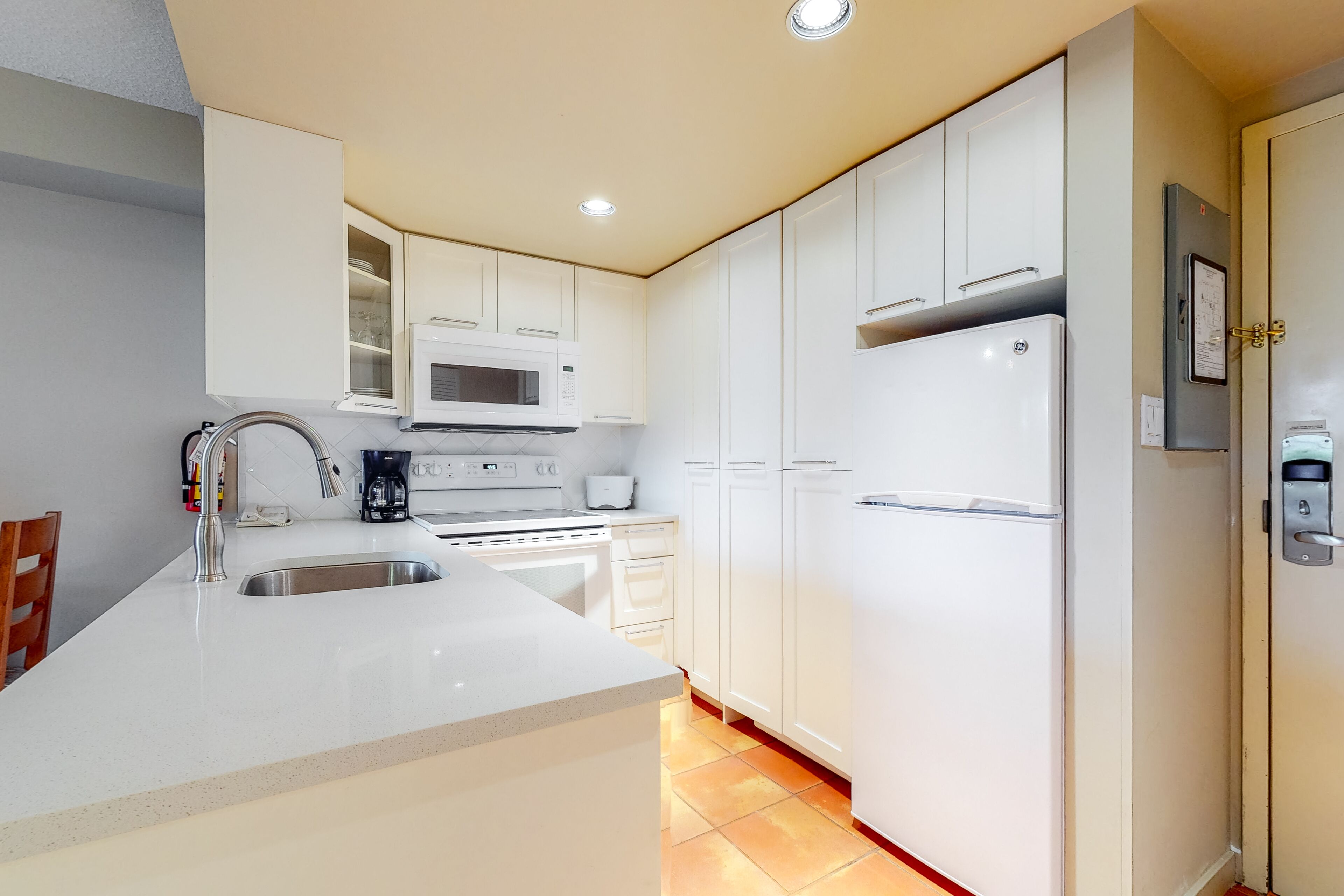 A modern kitchen with white cabinets, a built-in microwave, a refrigerator, and a stainless steel sink.