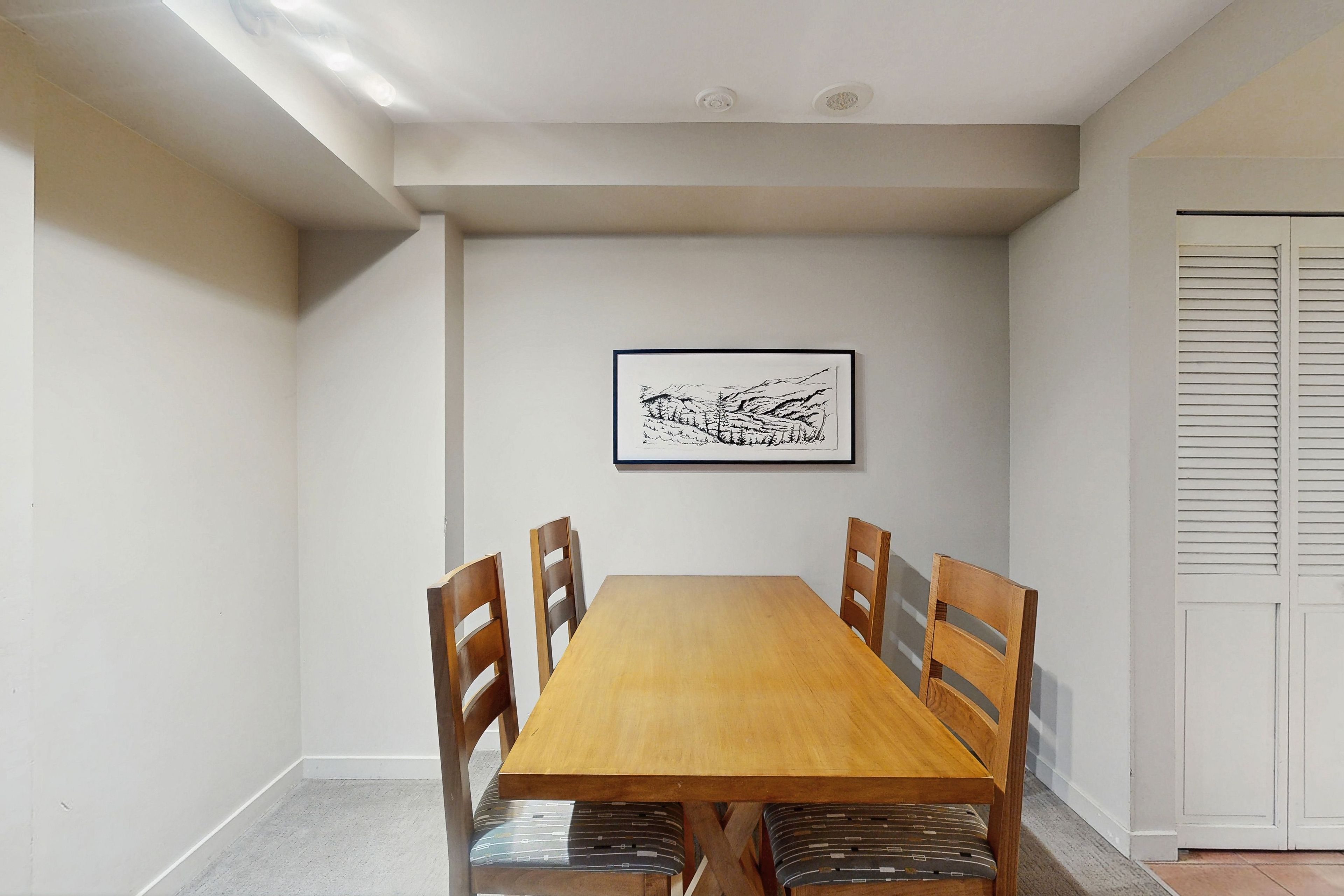 Un coin repas avec une table et des chaises en bois, un tableau encadré au mur et une porte à volets.