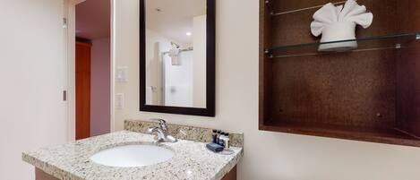 A bathroom with a granite countertop sink, a mirror, and a glass shelf with a towel.