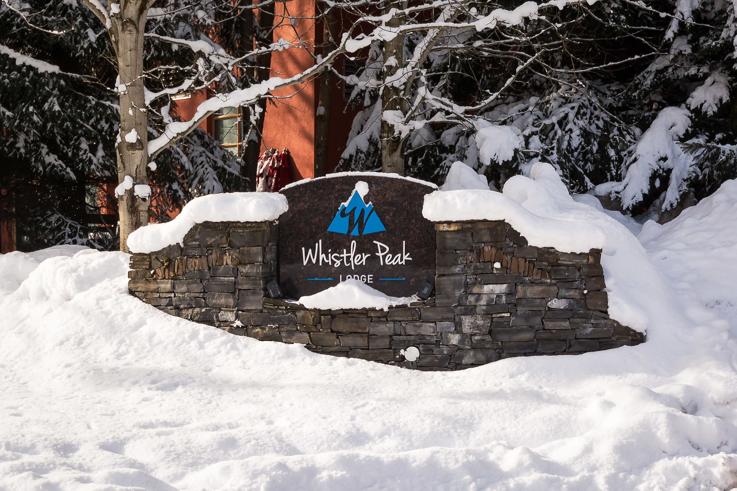 Un mur de pierre sur lequel est apposée une pancarte indiquant le « Whistler Peak Lodge », le tout étant entouré de neige.