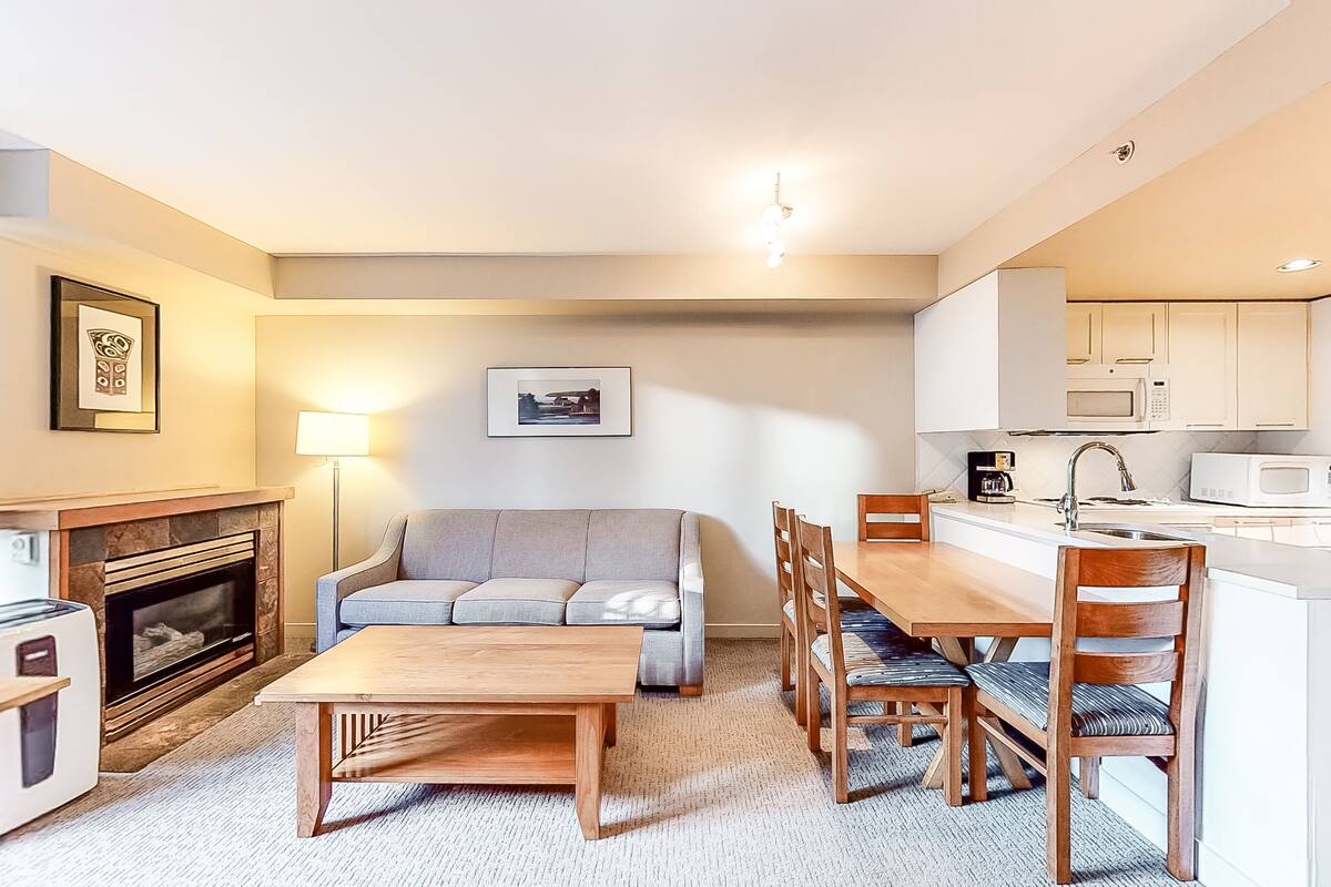 A compact living space with a sofa, dining table, chairs, a fireplace, a microwave, and a sink.