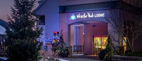 The exterior of Whistler Peak Lodge with a stone retaining wall, potted plants, and a snow-covered ground.