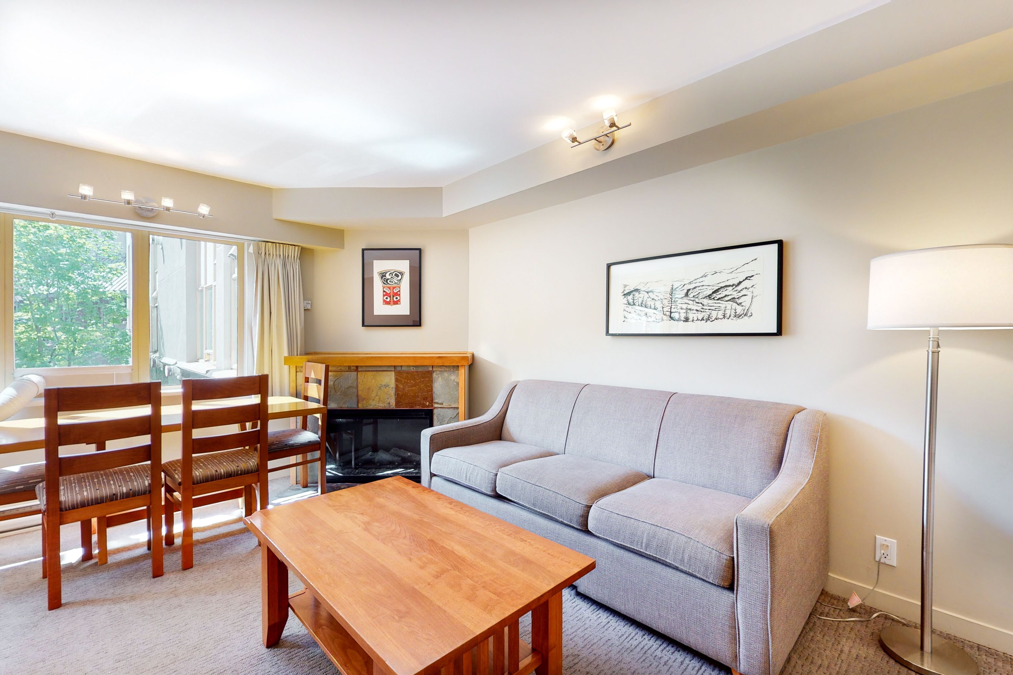A living room with a sofa, wooden table, chairs, a fireplace, and artwork on the walls.