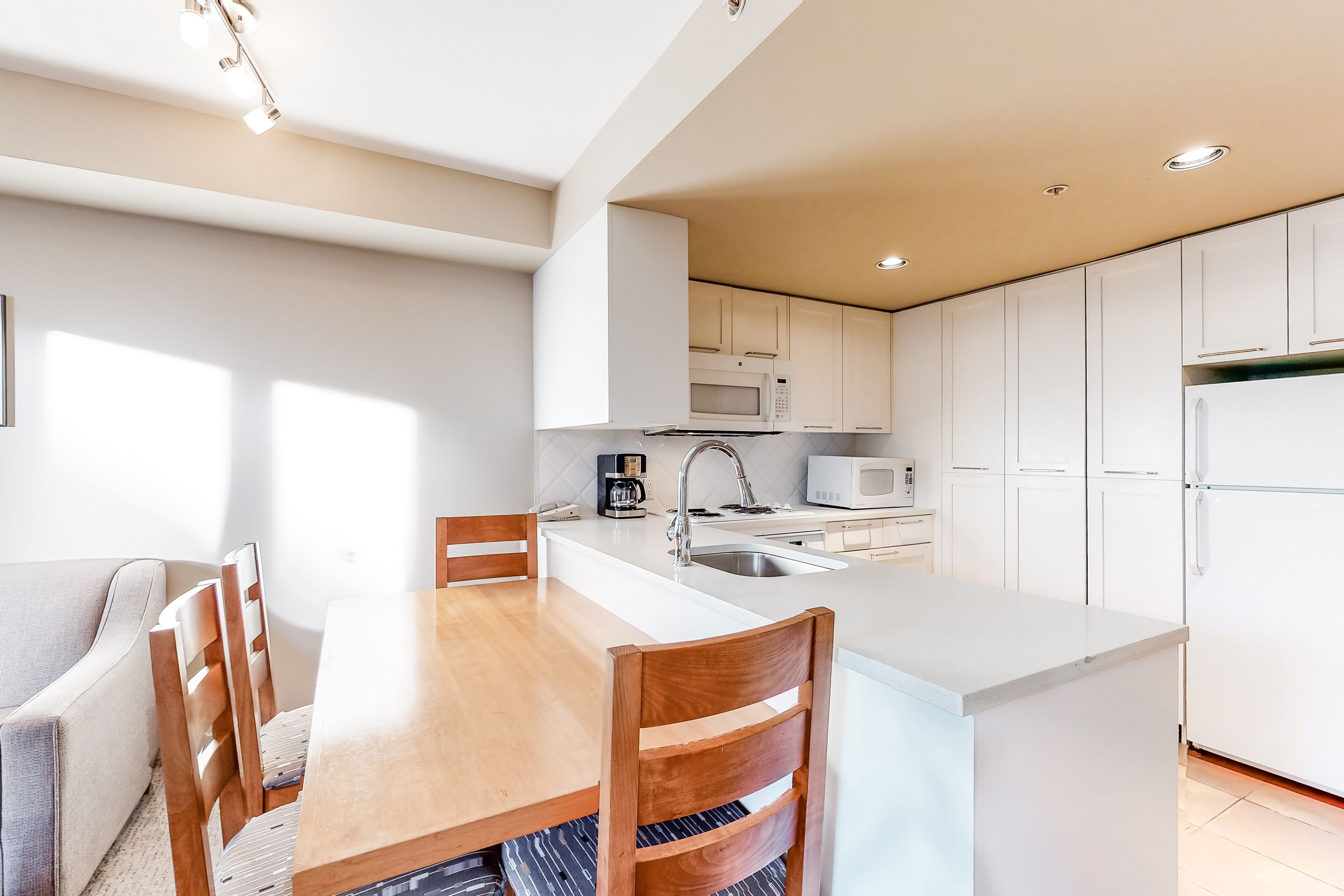 Una cocina moderna con armarios blancos, una isla central y una zona de comedor con sillas de madera.