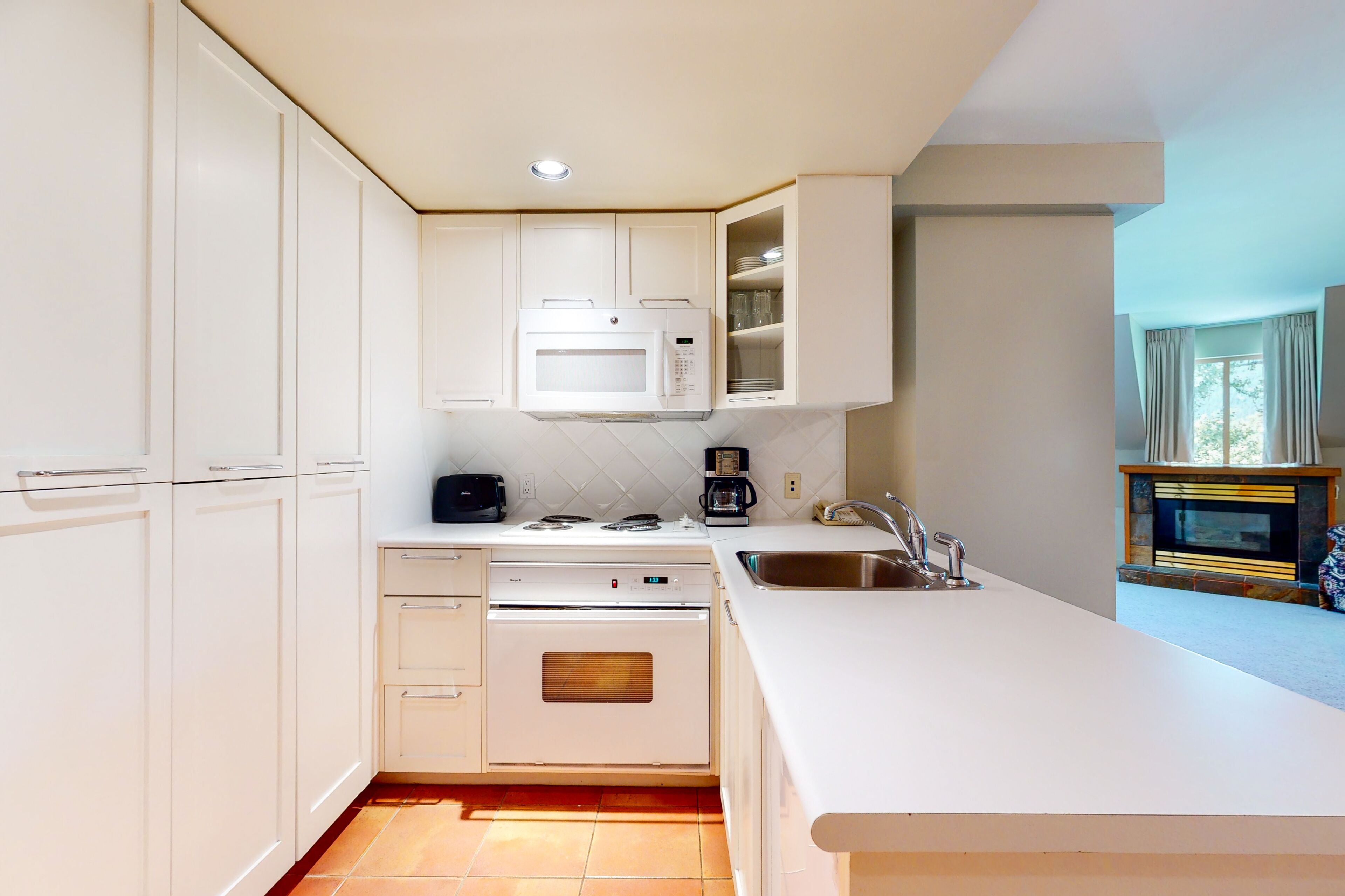 Una cocina moderna con armarios blancos, microondas integrado, cafetera y lavamanos.