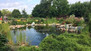 A pond surrounded by lush greenery and rocks, with a few people in the background. - Kouch Chalets (Saint Louis de Kent)