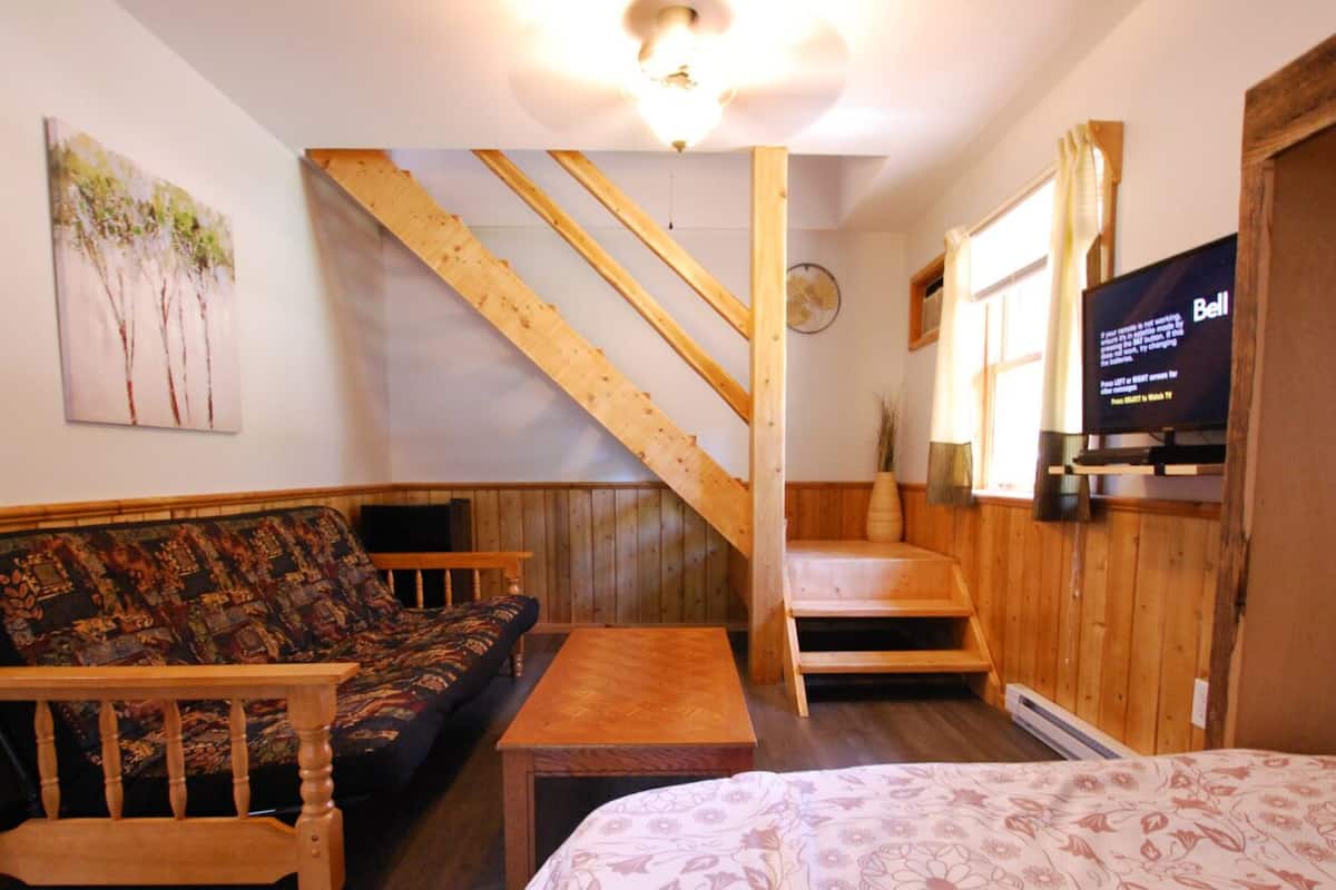 A cozy room with a wooden staircase, a sofa, a bed, and a television.