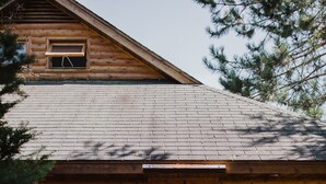 A wooden cabin with a red door, two windows, and a chimney. There are two Adirondack chairs outside. - Kouch Chalets (Saint Louis de Kent)