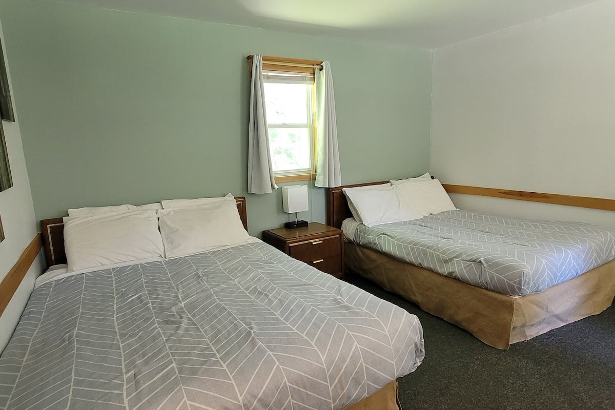 A room with two beds, a window with curtains, and a wall-mounted artwork.