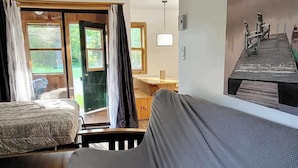 A spacious room with a large bed, a wooden desk, and a view of a wooden dock through a sliding door. - Kouch Chalets (Saint Louis de Kent)