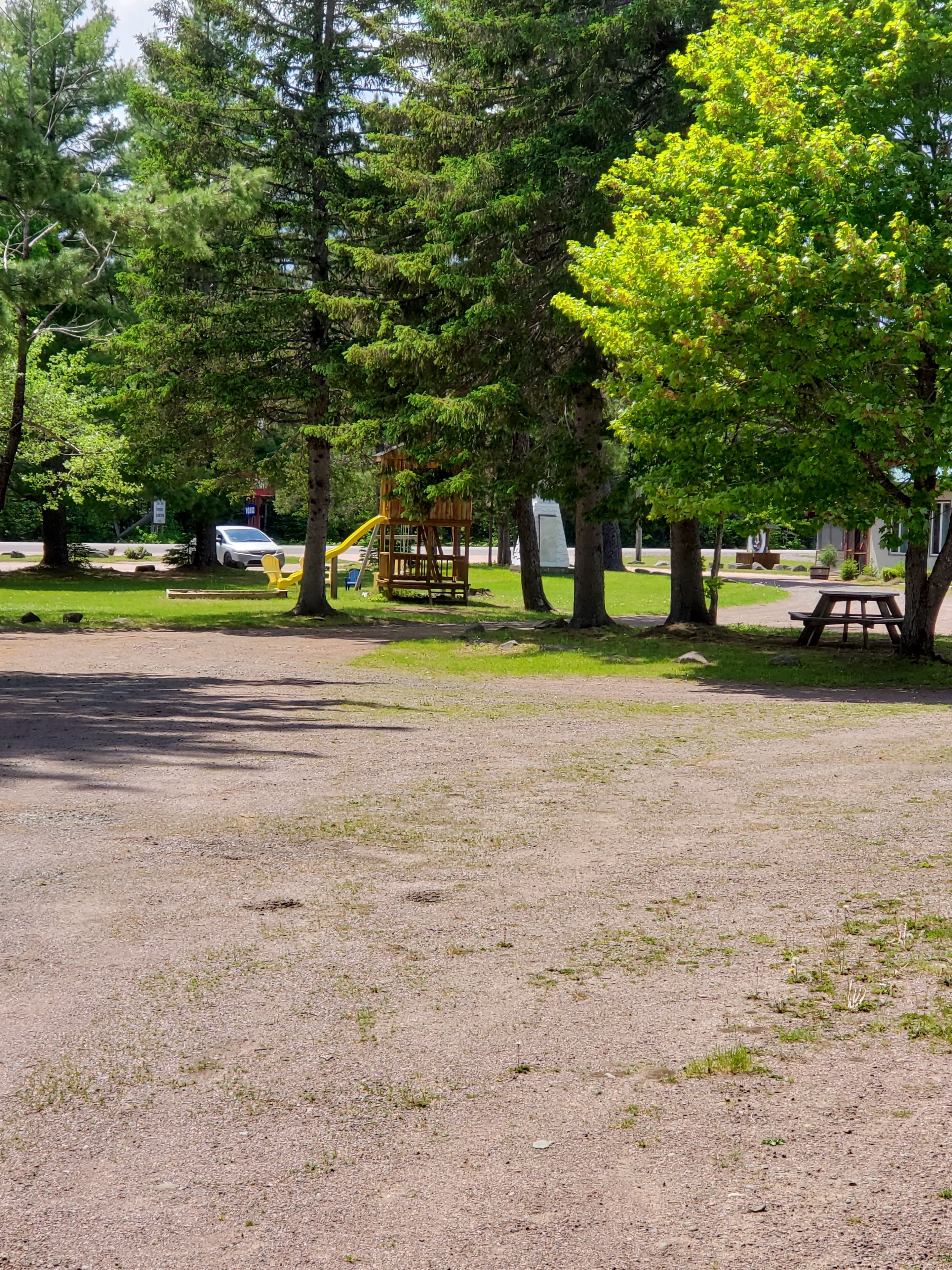 Un terrain de camping équipé de tables de pique-nique, d’une aire de jeux et d’un sentier de terre.