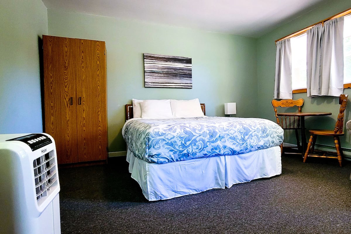 A room with a bed, a chair, a table, a heater, and a window with curtains.