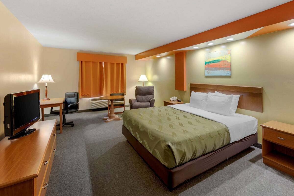 A hotel room with a bed, desk, chair, TV, and a painting on the wall.
