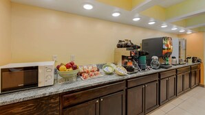 Una kitchenette con microondas, cafetera y refrigerador. Hay frutas y aperitivos en la encimera.