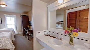 A hotel room with a large bed, a desk with a chair, a white sink, and a mirror.