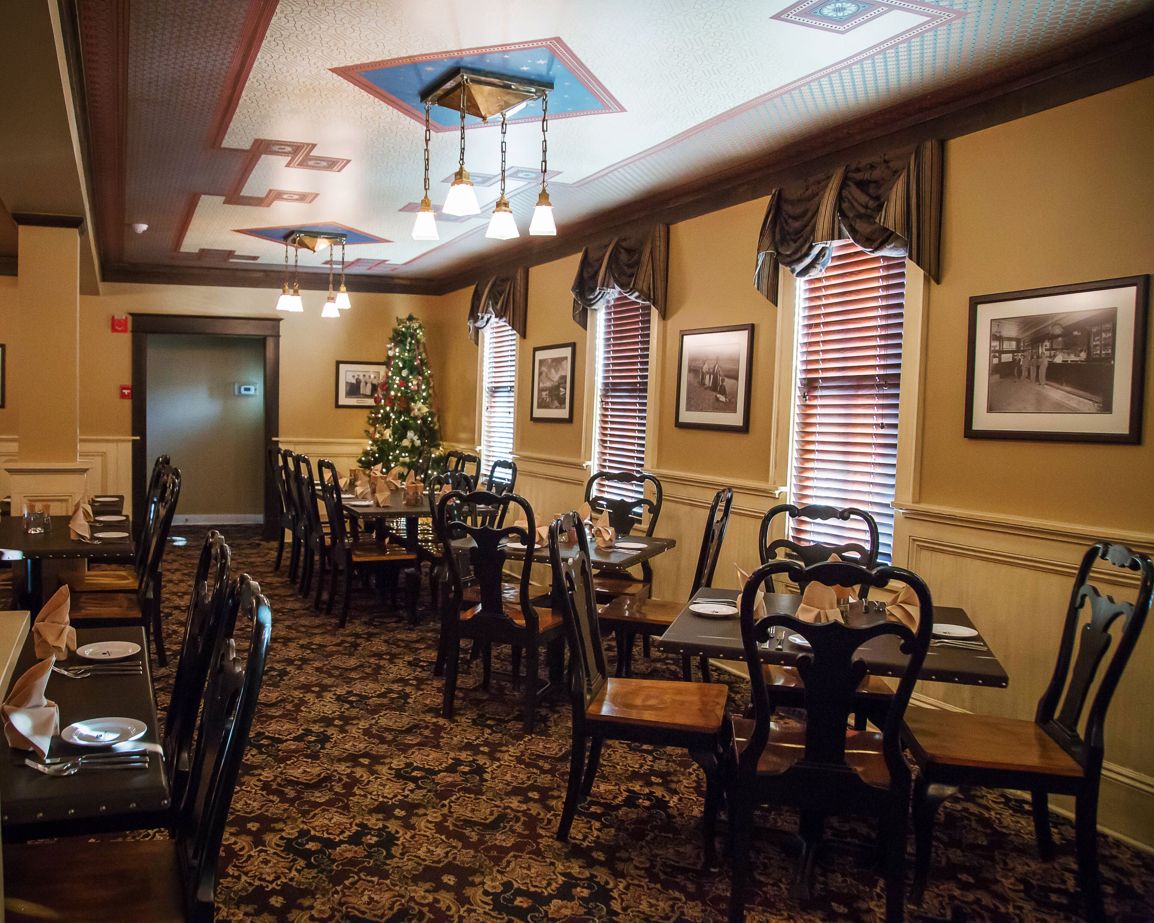 A dining area with tables and chairs, a Christmas tree, and framed pictures on the walls.